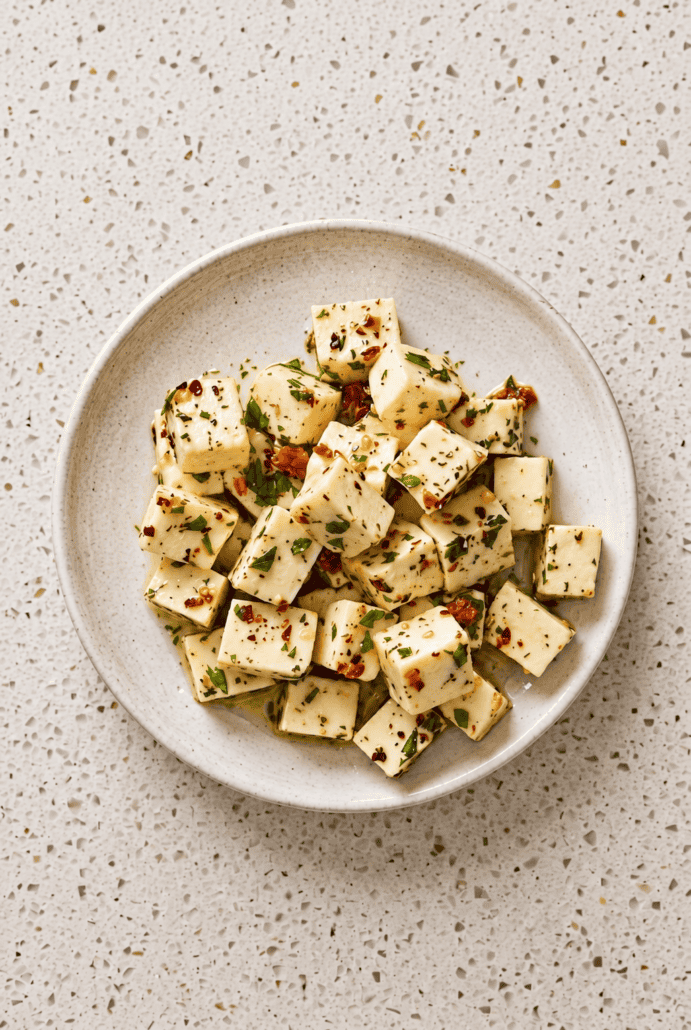 Marinated mozzarella cubes coated with herbs and red pepper flakes, served as an easy Italian appetizer.
