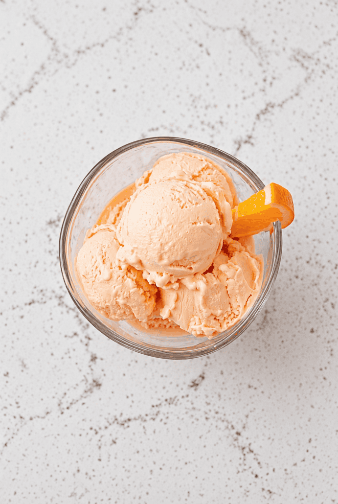 Scoops of homemade orange ice cream topped with a fresh orange slice.
