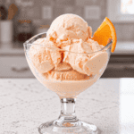 Creamy homemade orange ice cream scoops with fresh orange slice garnish.