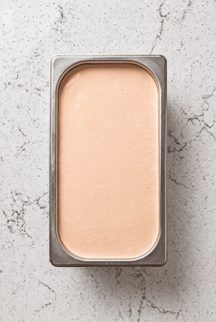 Orange ice cream mixture in a freezer-safe container ready to freeze.