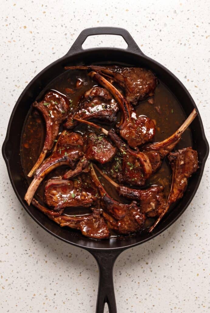 Pomegranate lamb chops coated in a rich glaze and cooking in a cast iron skillet.