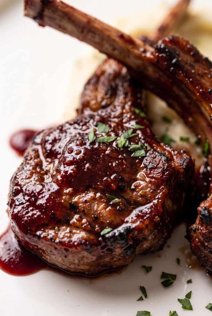Glazed pomegranate lamb chop topped with fresh herbs and served with pomegranate seeds.