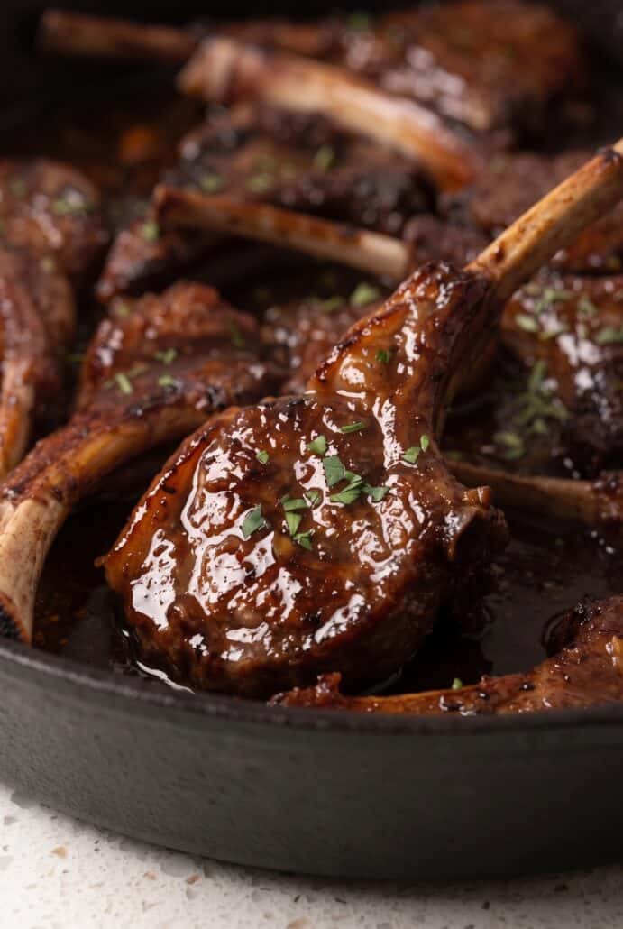 Close-up of pomegranate lamb chops coated in a glossy sauce and sprinkled with fresh herbs.