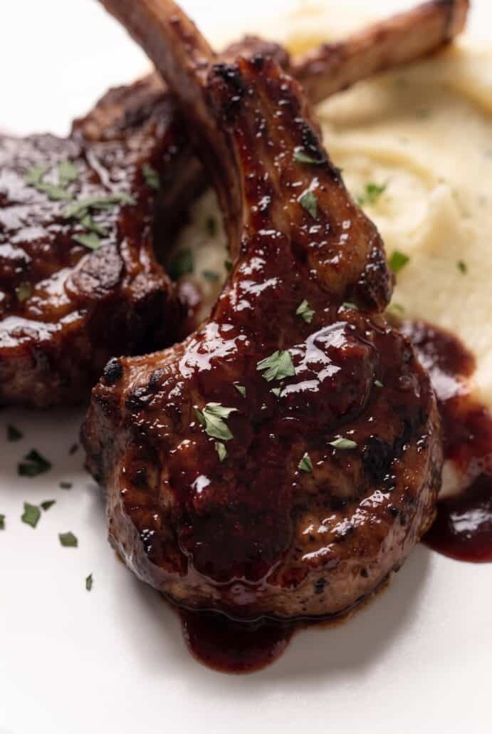 Pomegranate lamb chops with glossy glaze, fresh herbs, and creamy mashed potatoes.